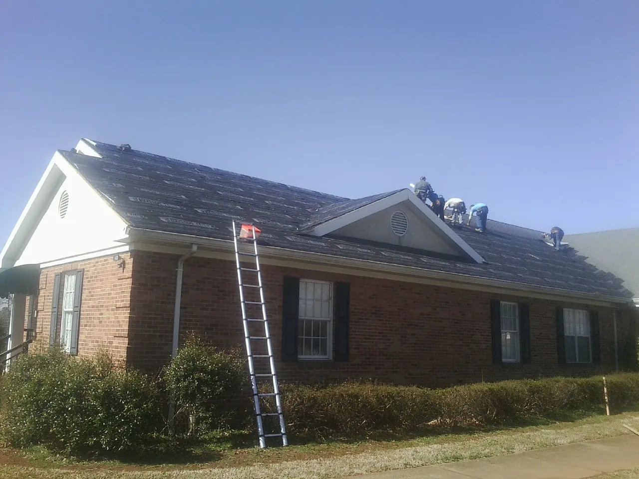 Crew tearing shingles off a brick ranch roof with a ladder set — Metal Roof Repair work by our crew in Merrimac