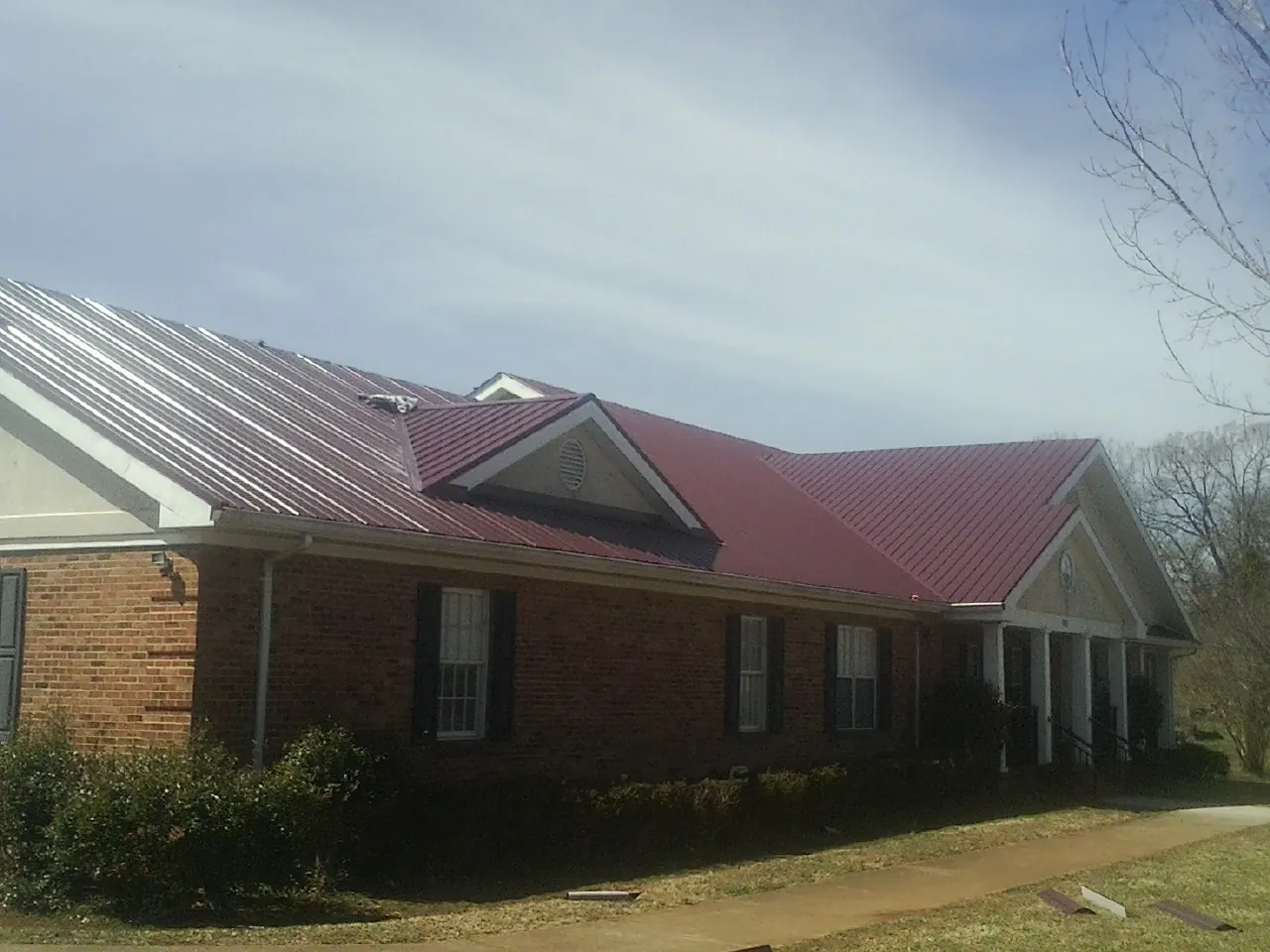 Red metal roof with gabled entries on a long brick building, from a Hail Damage Roof Repair job in Merrimac
