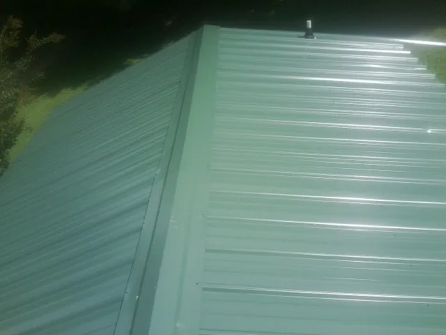 New green metal panels meeting at the ridge of a roof — Flat Roof Repair work by our crew in Merrimac