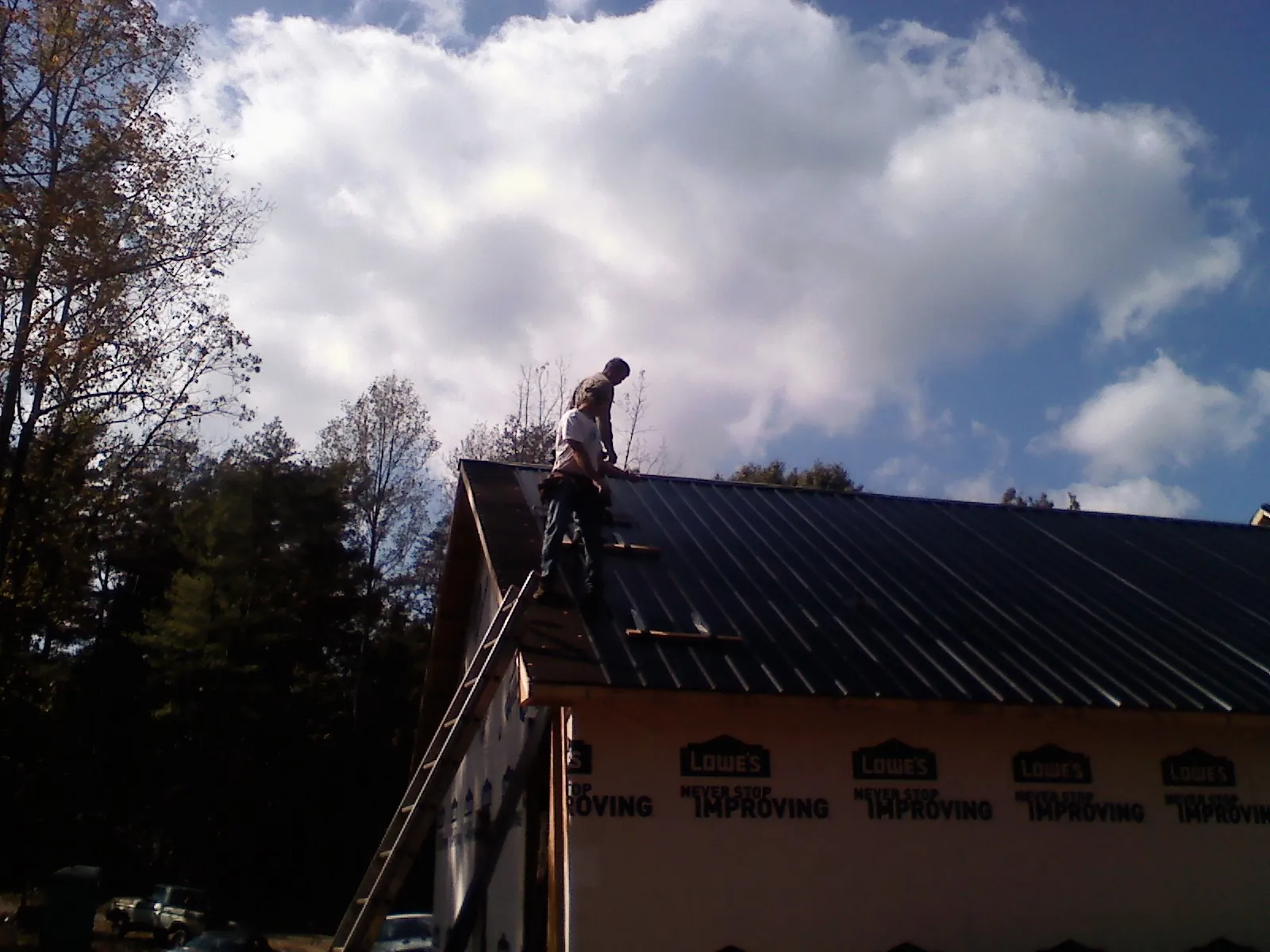 Roofer fastening dark metal panels high against a cloudy sky, from a Roof Inspection job in Merrimac